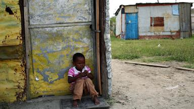Afrikanischer Junge sitzt alleine in einem armen Dorf