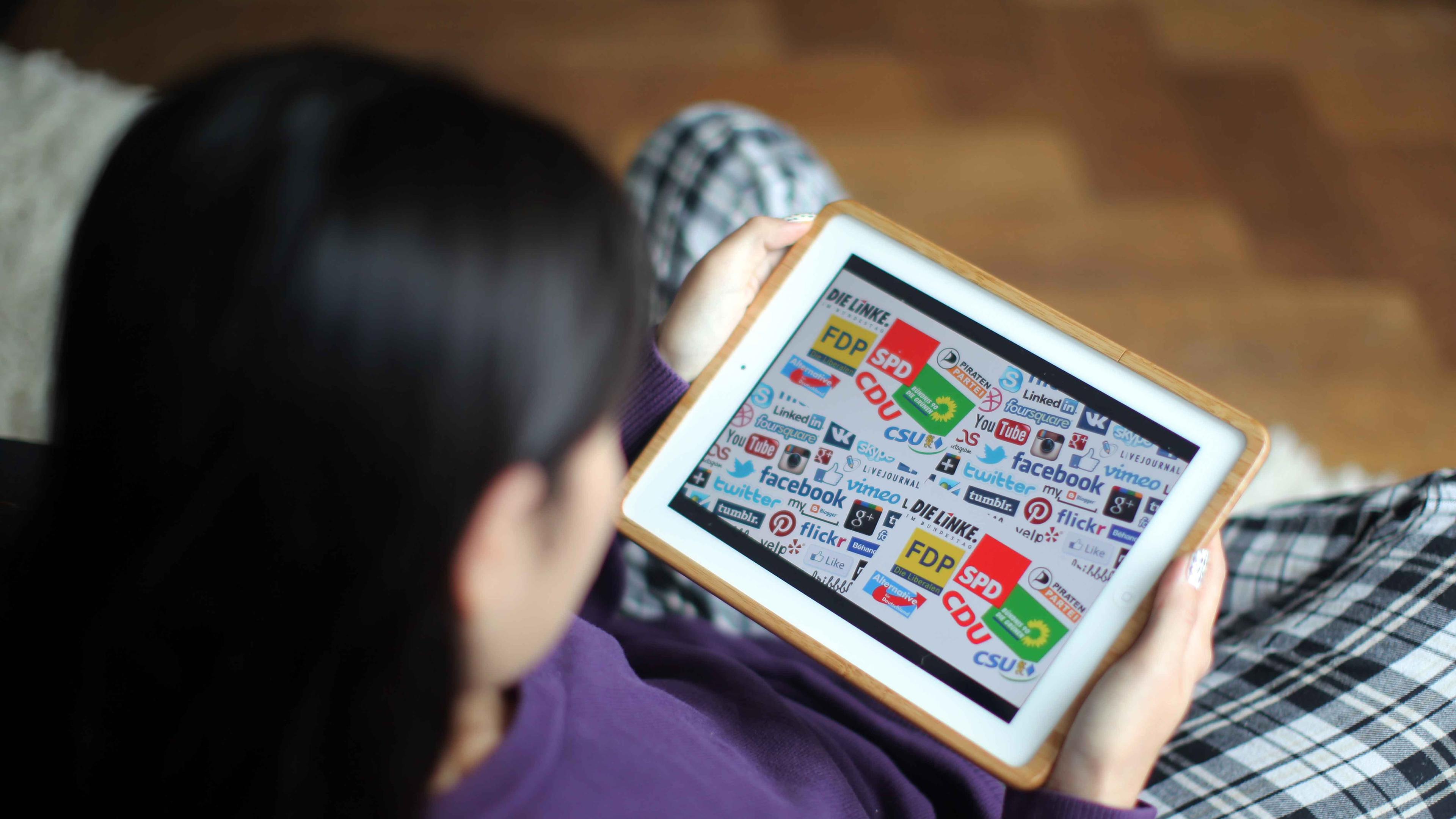 Junge Frau schaut auf ein Tablet mit Parteien-Logos.