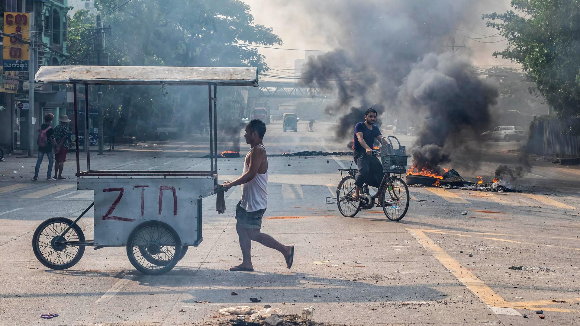 Ein Radfahrer fährt in Myanmar an Barikaden und brennenden Autoreifen vorbei