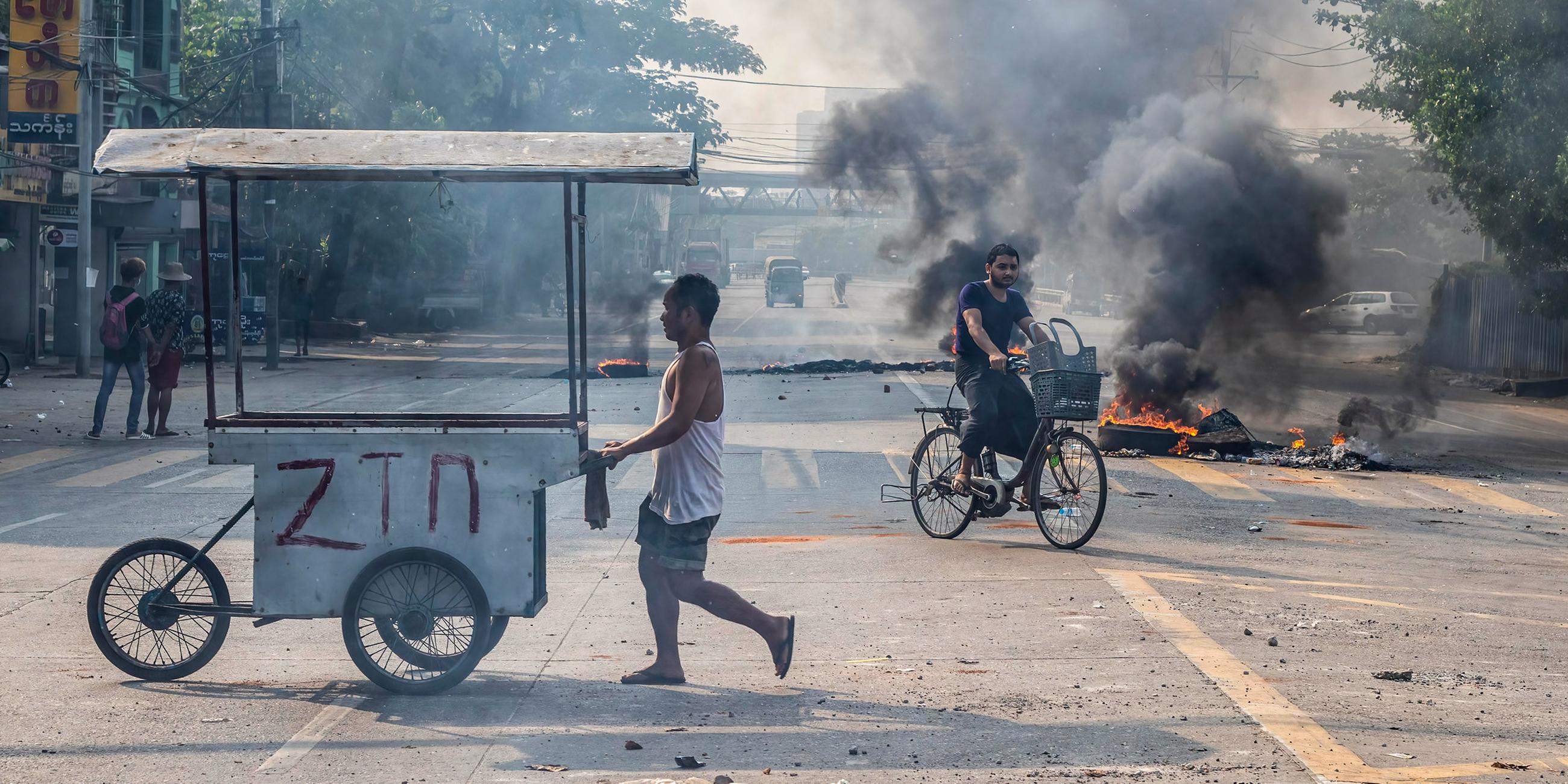 Ein Radfahrer fährt in Myanmar an Barikaden und brennenden Autoreifen vorbei