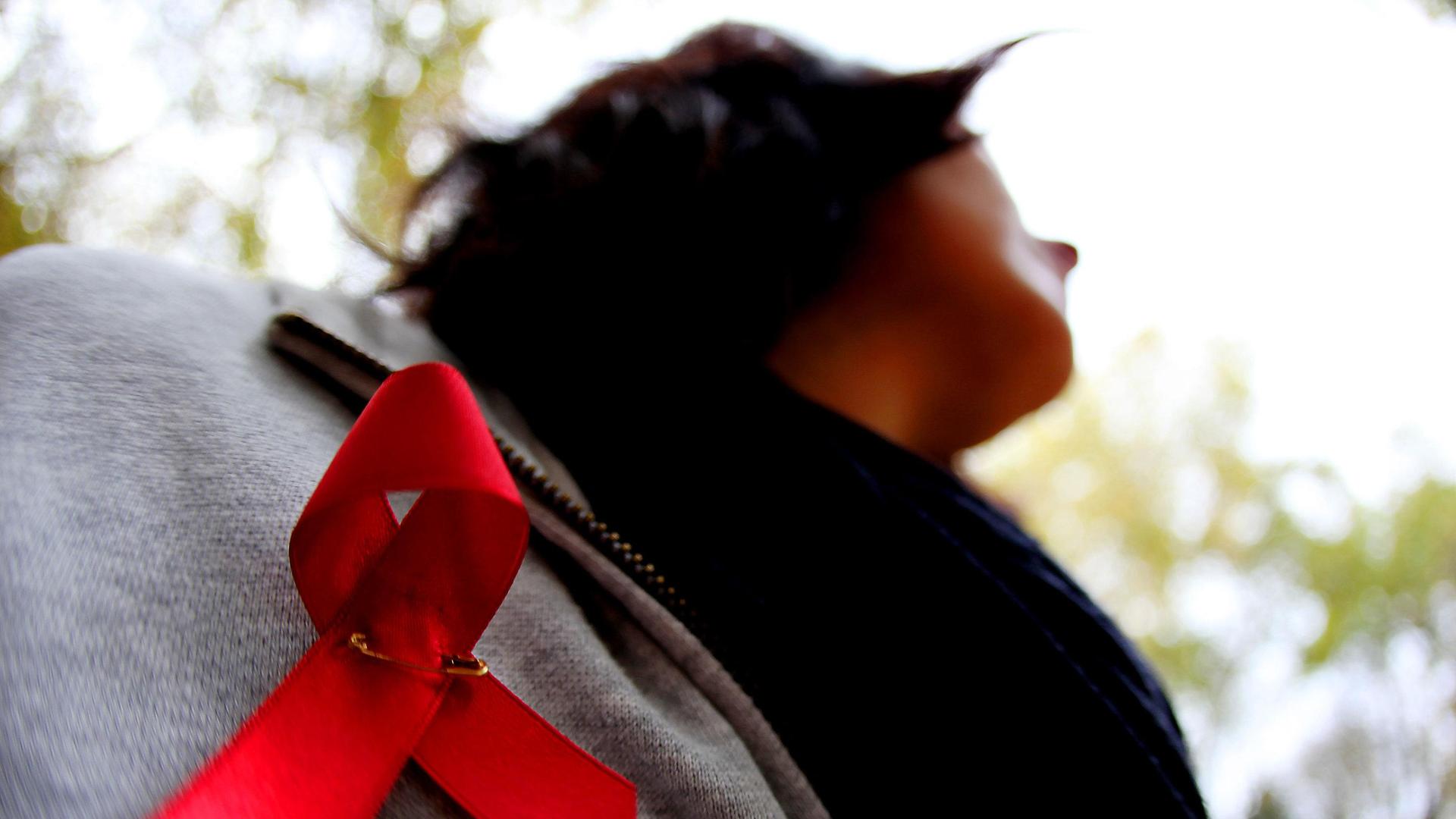 Einf Frau hat eine rote Aids-Schleife angesteckt.
