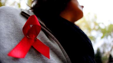 Einf Frau hat eine rote Aids-Schleife angesteckt.