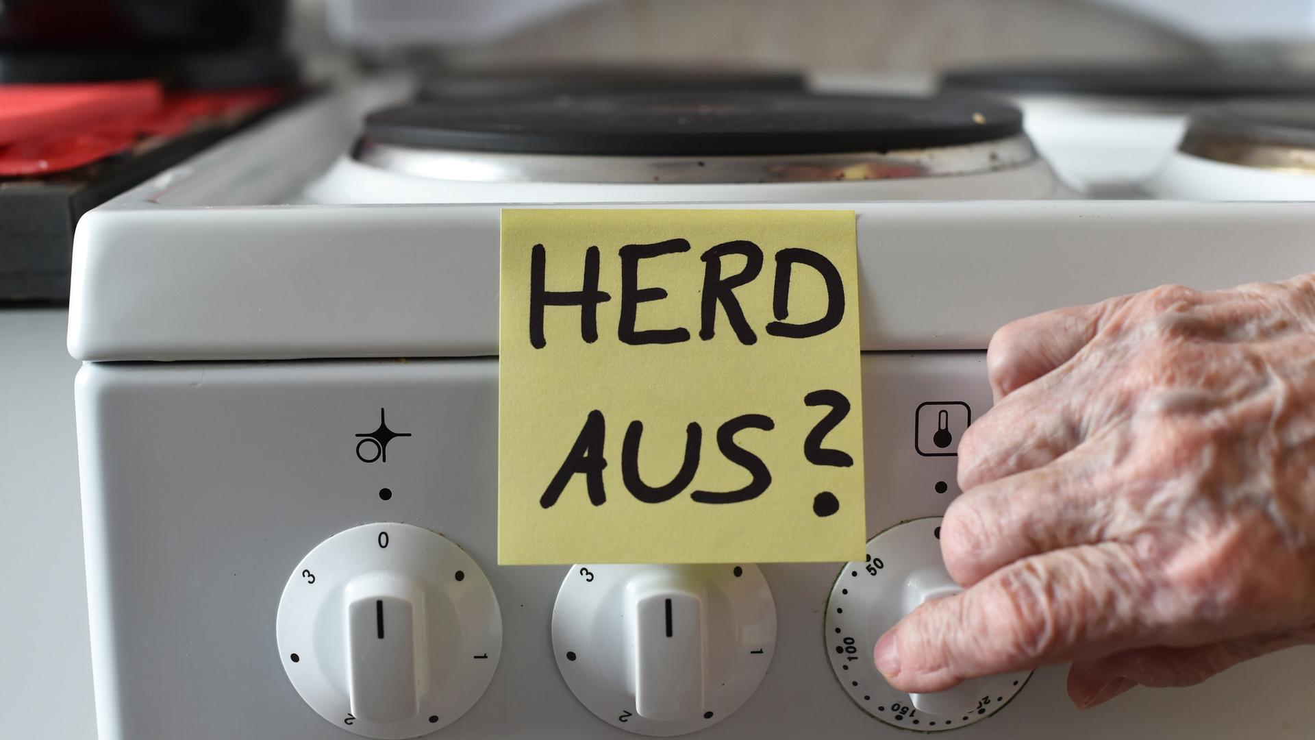 Post-it mit Aufschrift "Herd aus?" hängt am Herd, alte Frauenhand macht Herd aus 