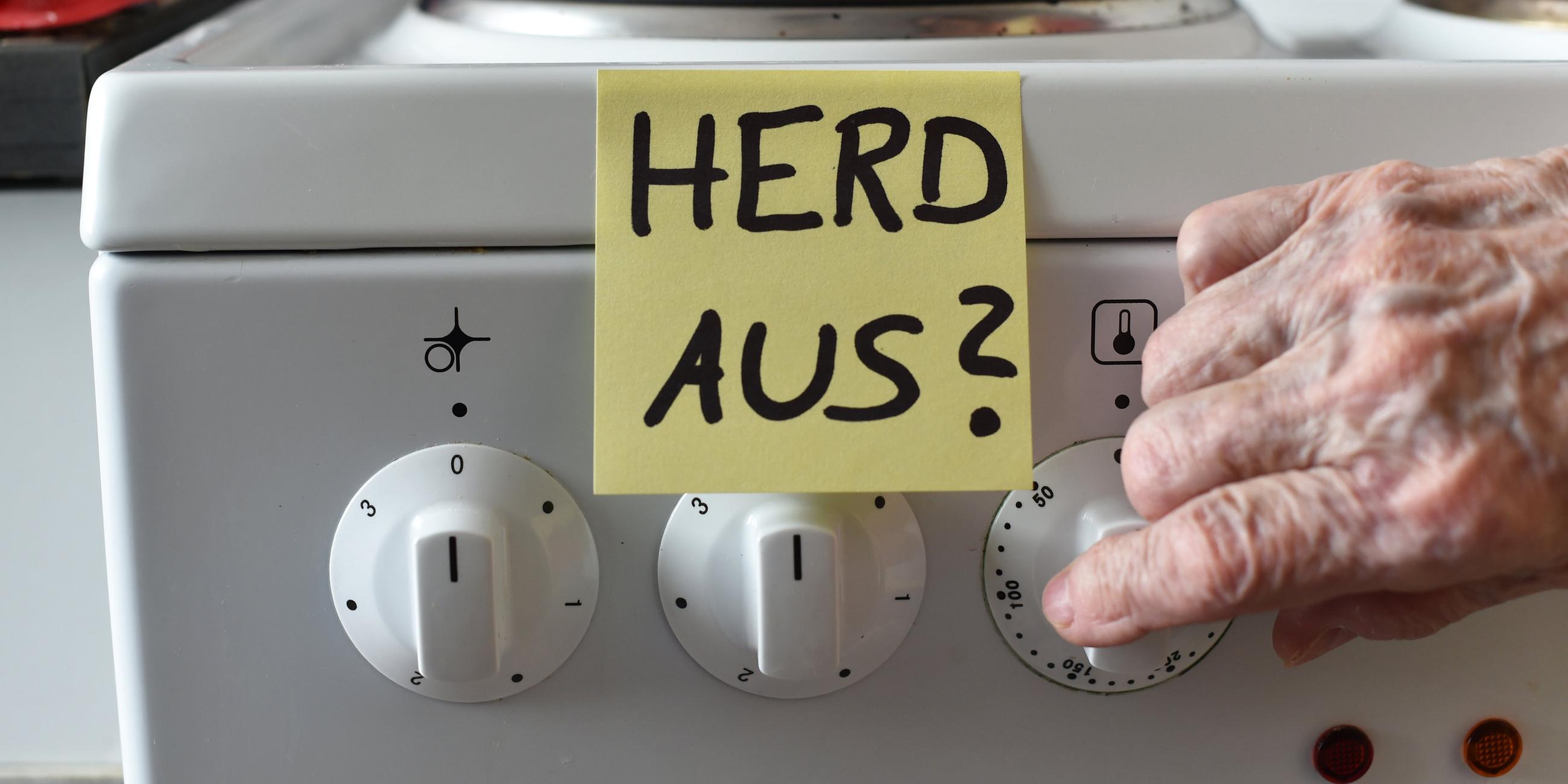 Post-it mit Aufschrift "Herd aus?" hängt am Herd, alte Frauenhand macht Herd aus 
