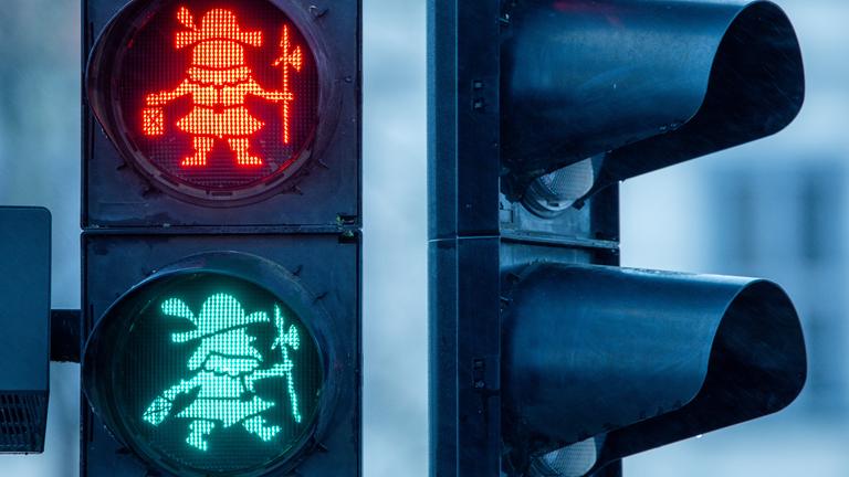 Das rote und grüne Feld einer Ampel leuchten, das Ampelmännchen ist eine Figur mit Hellebarde und Hut.