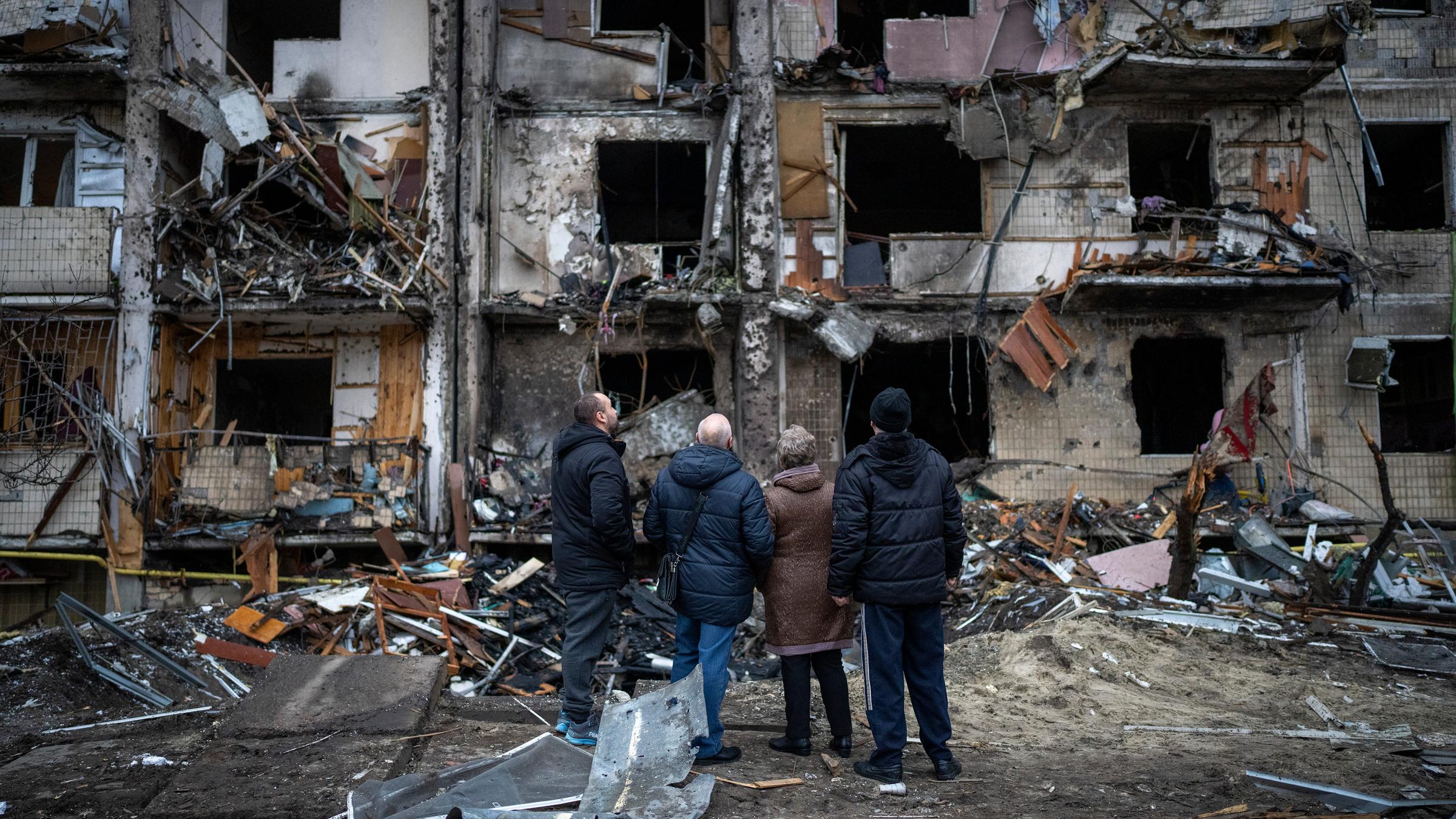 Vier Menschen stehen vor einem völlig zerstörten Wohnblock
