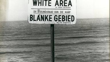 Schwarzweißfoto: Ein Schild mit der Aufschrift "White Area" steht an einem Strand.