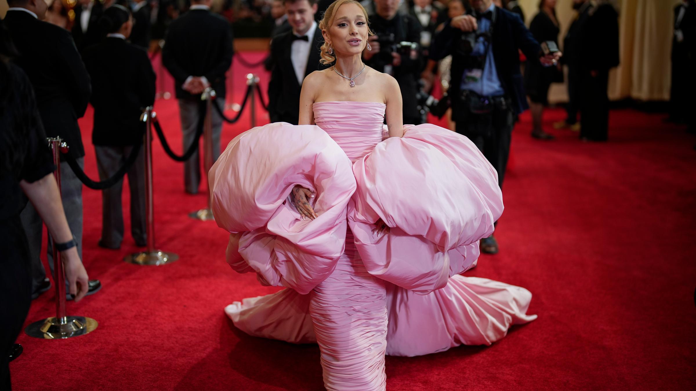 Ariana Grande posiert auf dem roten Teppich in einem pompösen rosanen Kleid.