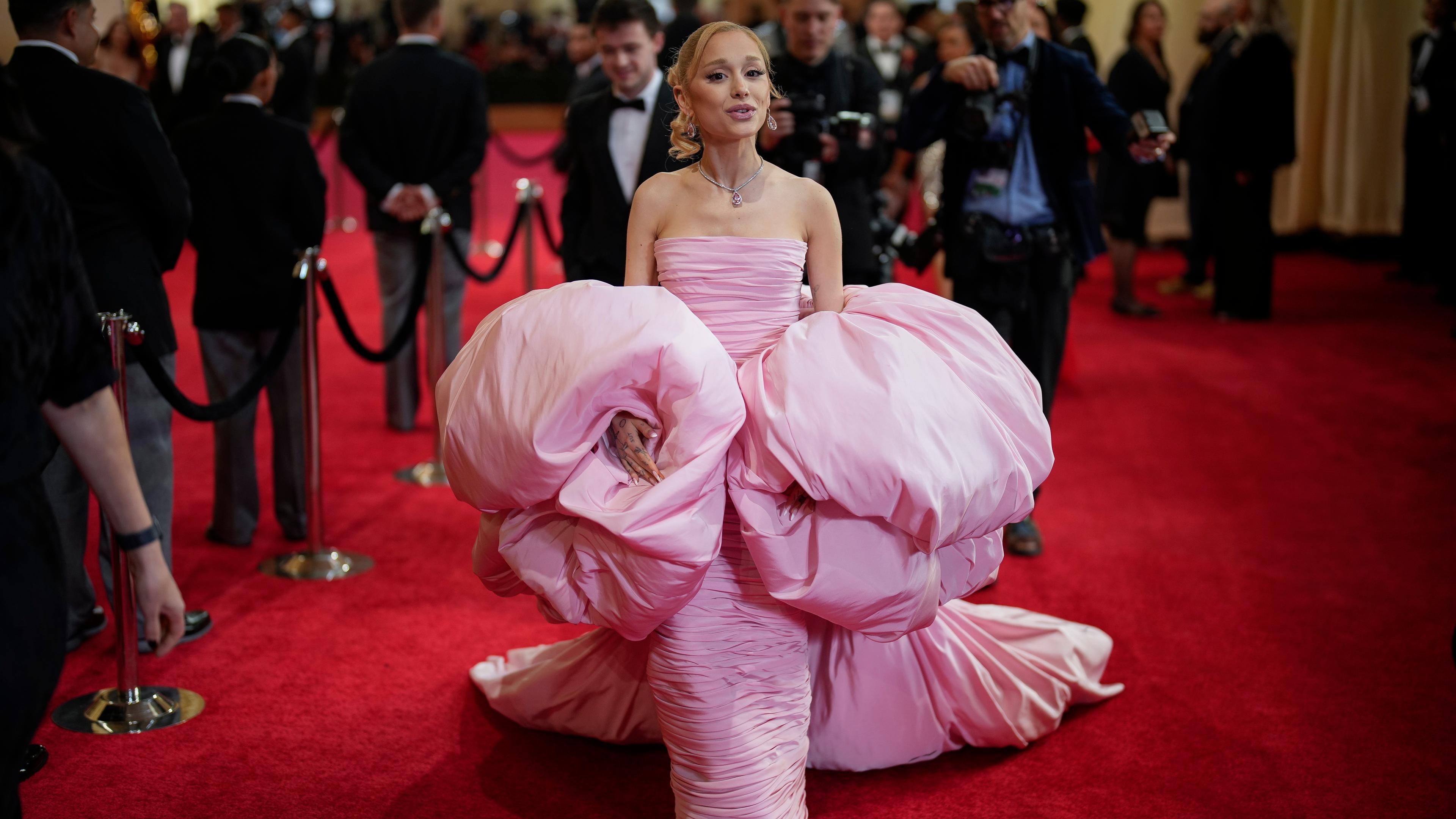 Ariana Grande posiert auf dem roten Teppich in einem pompösen rosanen Kleid.