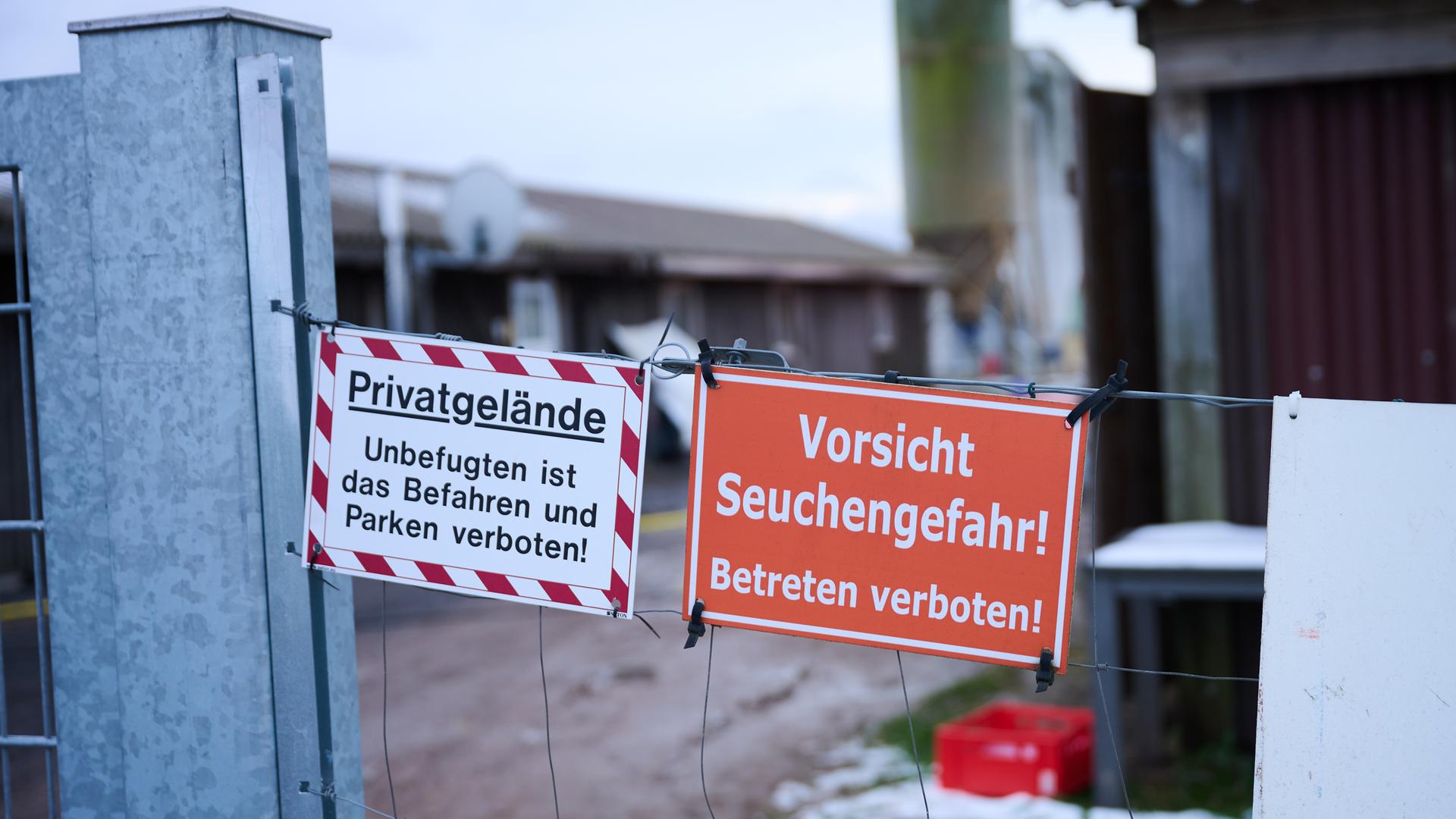 Ein Absperrdraht mit zwei Warnschildern. Auf dem einen steht auf weißem Untergrund "Privatgelände - Unbefugten ist das Parken und Betreten verboten!" auf dem anderen steht auf rotem Untergrund "Vorsicht Seuchengefahr - Betreten verboten!". Im Hintergrund ist ein landwirtschaftlicher Betrief unscharf zu erkennen. 
