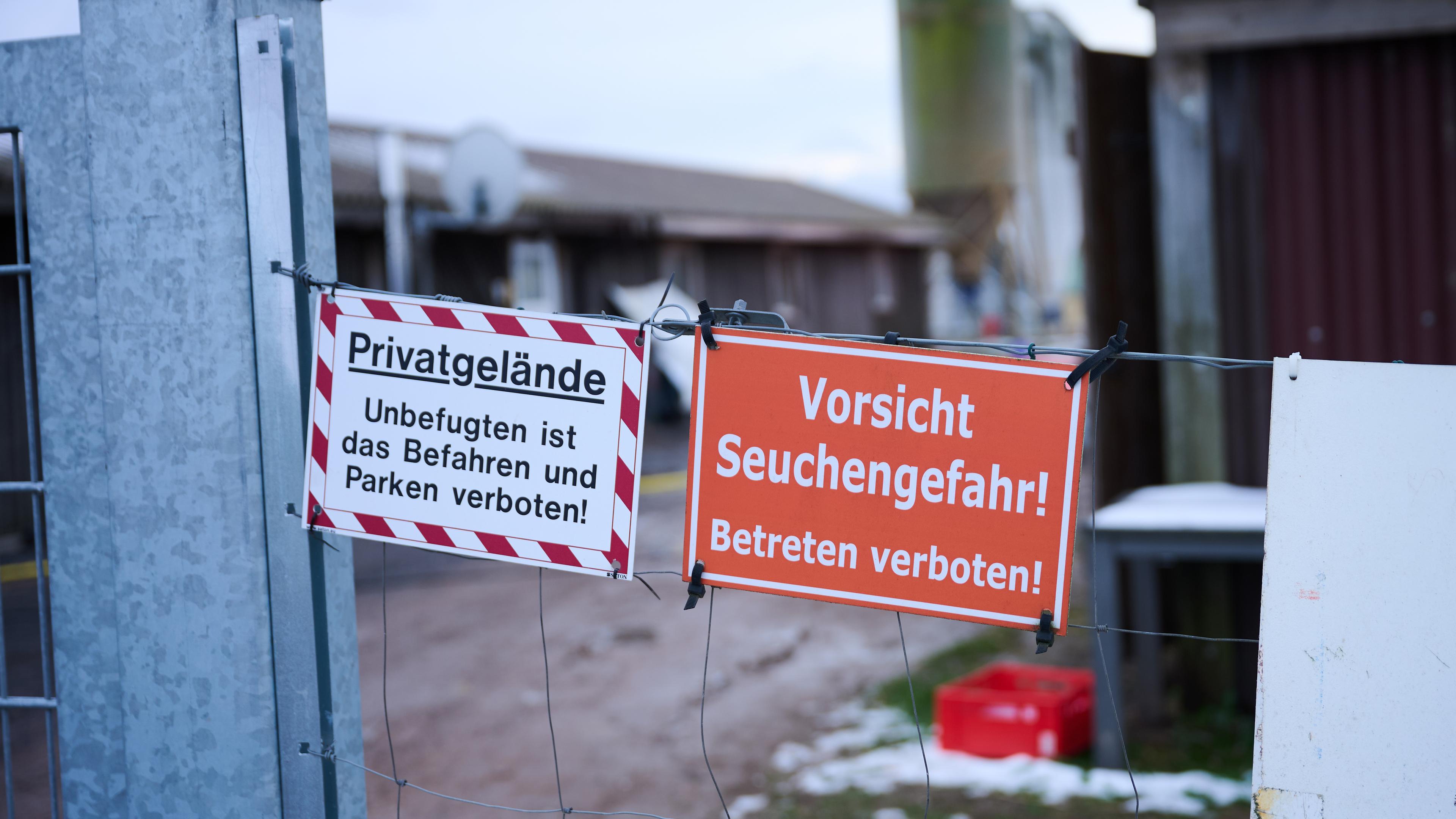 Ein Absperrdraht mit zwei Warnschildern. Auf dem einen steht auf weißem Untergrund "Privatgelände - Unbefugten ist das Parken und Betreten verboten!" auf dem anderen steht auf rotem Untergrund "Vorsicht Seuchengefahr - Betreten verboten!". Im Hintergrund ist ein landwirtschaftlicher Betrief unscharf zu erkennen. 