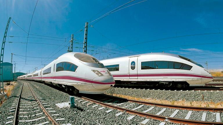 Zwei Züge vom Typ AVE 103 stehen auf den Gleisen. Sie sind weiß und haben einen dünnen dunkelroten Streifen an der Seite.