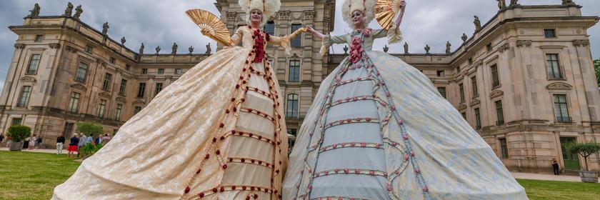 Nach langer Renovierung wird das Barockschloss Ludwigslust wieder eröffnet. Zur Feier laufen kunstvoll verkleidete Stelzenläuferinnen durch den Park.