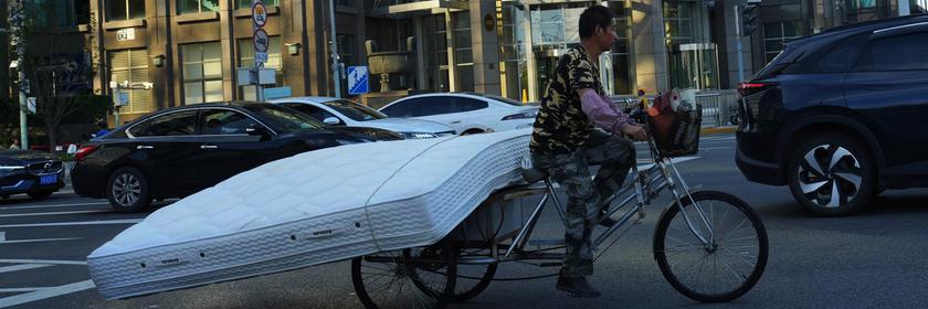 Ein Mann fährt in Peking mit einem Dreirad, um eine Matratze zu transportieren.