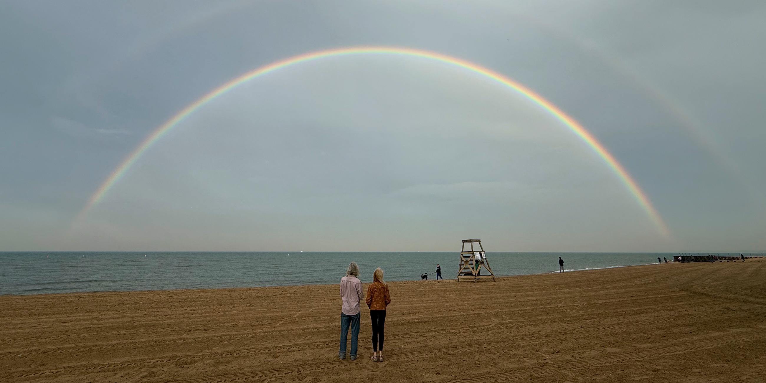 Menschen stehen am Strand von Chicago und schauen auf doppelten Regenmogen am Himmel