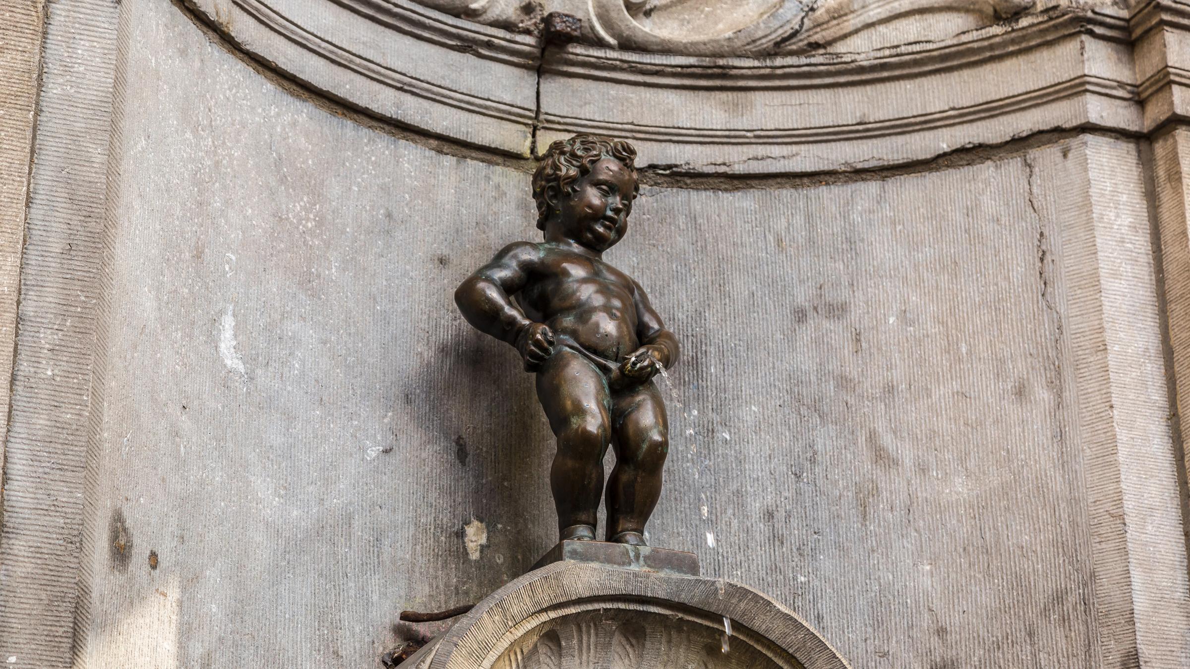Eine Figur steht auf einem Sockel und pinkelt in einen Brunnen
