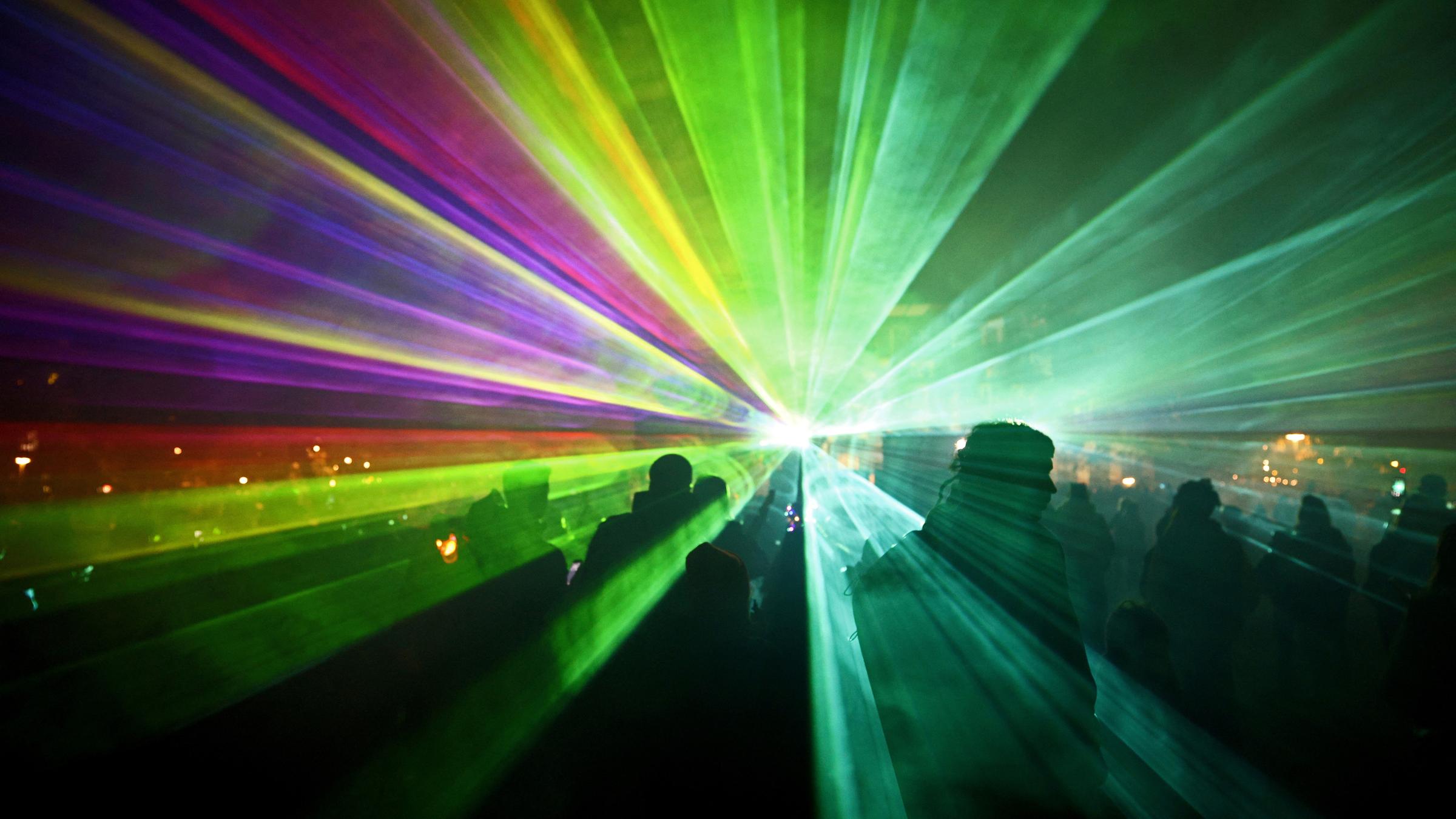 Bunte Lichter leuchten direkt in die Kamera, Leute stehen davor.