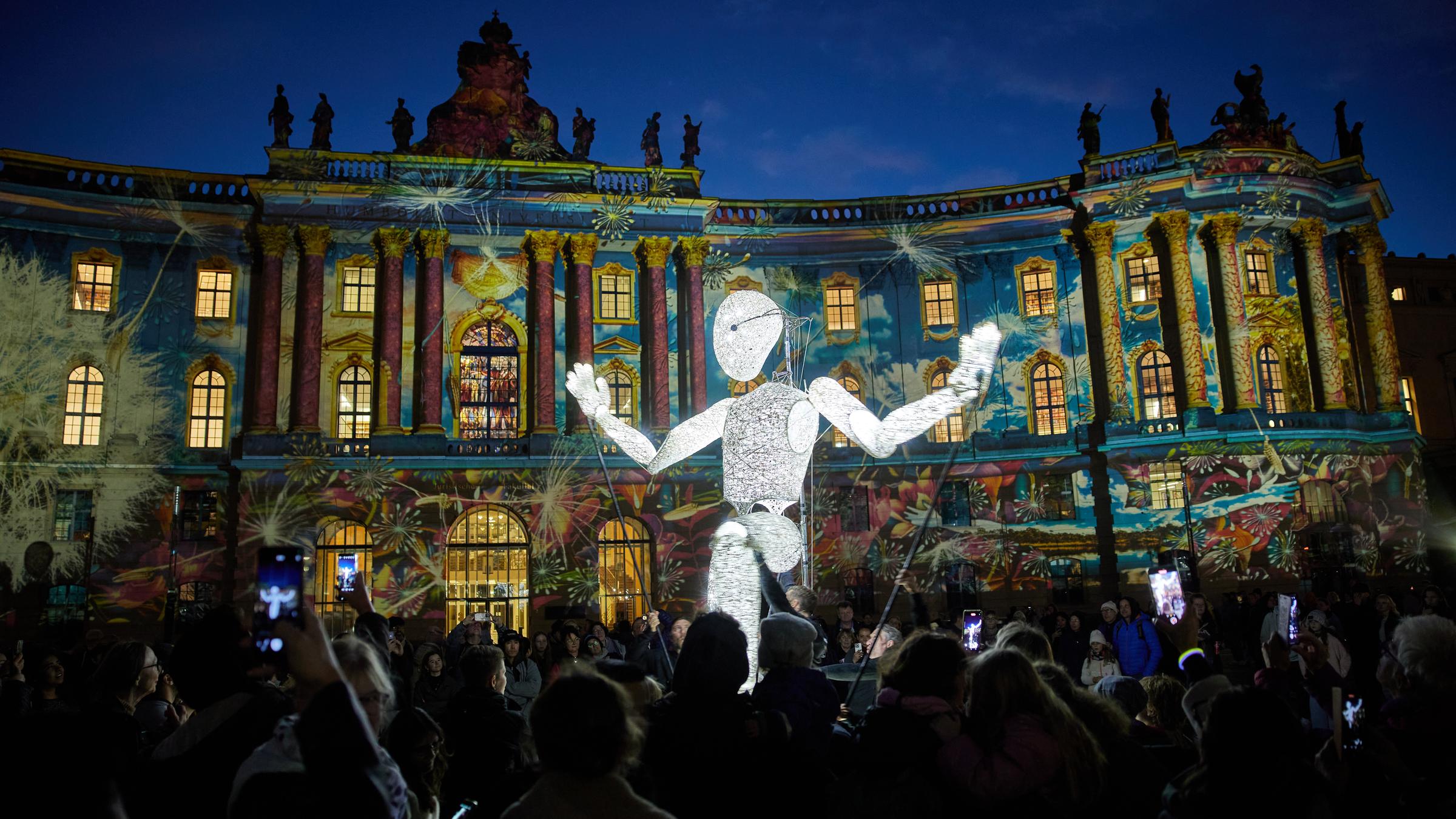 Eine riesige leuchtende Figur in weiß steht in einer Menschenmenge.