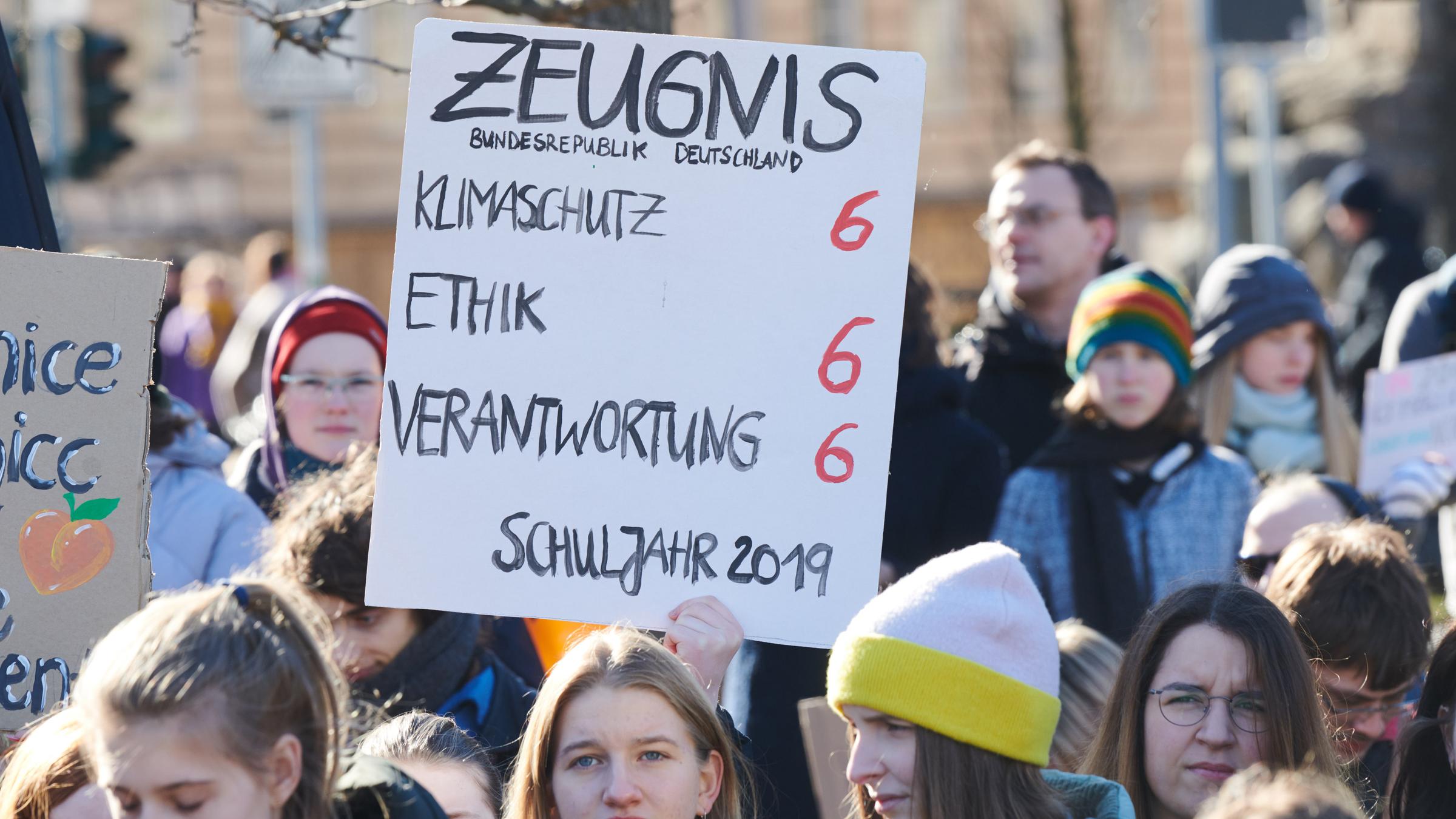 Demonstranten halten ein Plakat hoch mit der Aufschrift "Zeugnis für die Bundesrepublik Deutschland". In den Bereichen Klimaschutz, Ethik und Verantwortung gibt es Sechsen.