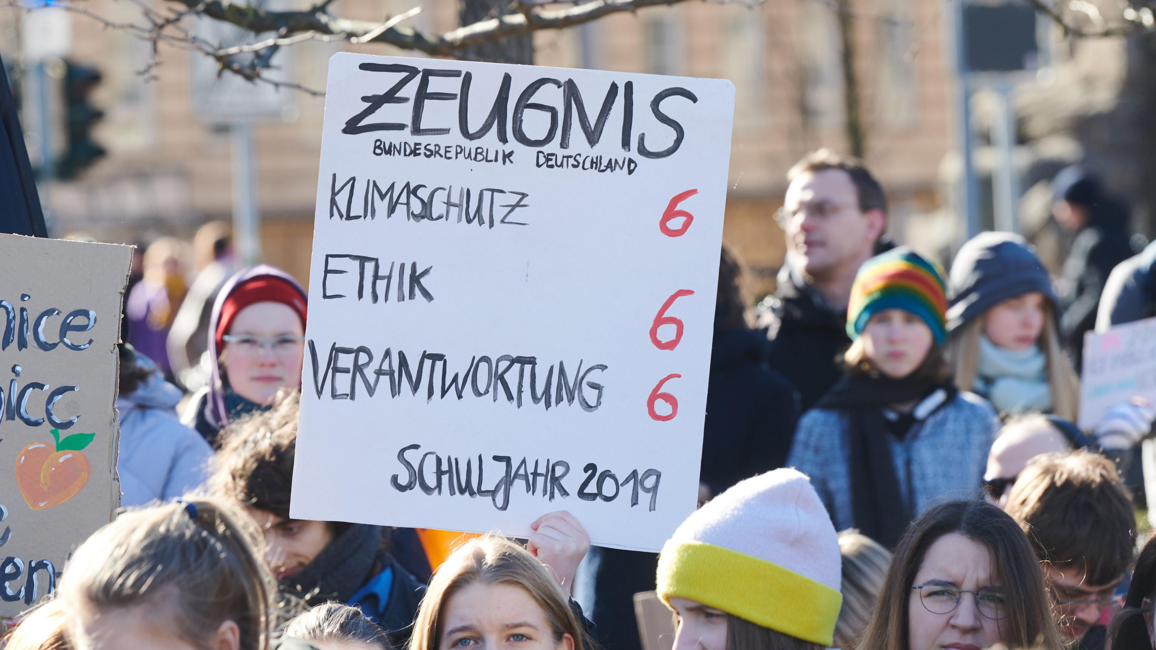 Demonstranten halten ein Plakat hoch mit der Aufschrift "Zeugnis für die Bundesrepublik Deutschland". In den Bereichen Klimaschutz, Ethik und Verantwortung gibt es Sechsen.