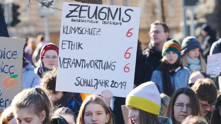 Demonstranten halten ein Plakat hoch mit der Aufschrift "Zeugnis für die Bundesrepublik Deutschland". In den Bereichen Klimaschutz, Ethik und Verantwortung gibt es Sechsen.