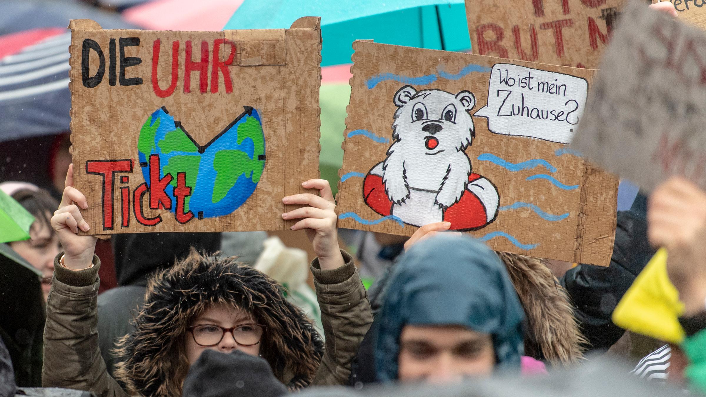 Schüler halten zwei Plakate hoch. Das Eine zeigt die Erde als Uhr mit der Aufschrift "Die Uhr tickt". Auf dem zweiten Plakat ist ein Eisbär im Schwimmring mit Sprechblase aufgemalt: Er fragt: "Wo ist mein Zuhause?"