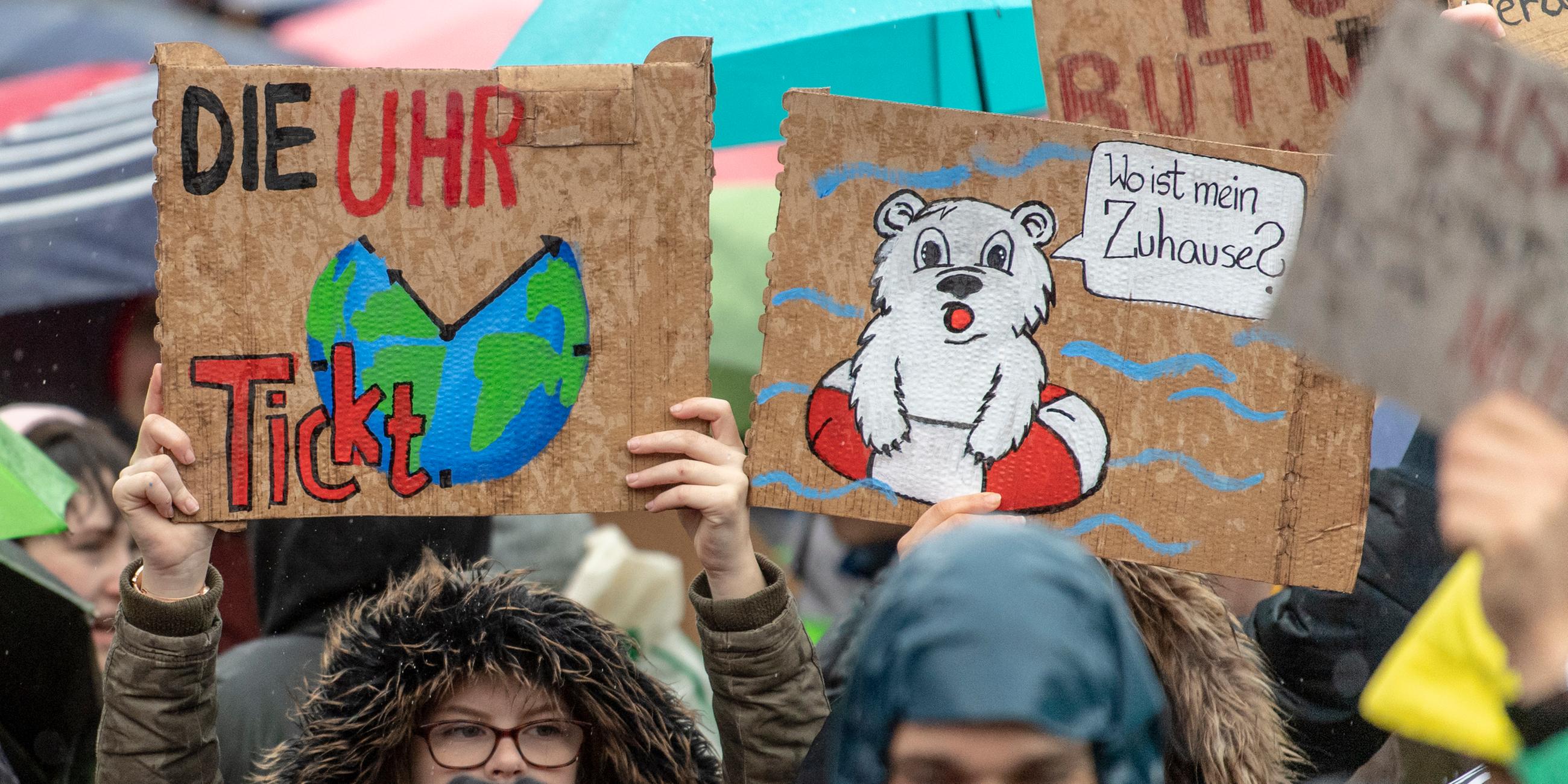 Schüler halten zwei Plakate hoch. Das Eine zeigt die Erde als Uhr mit der Aufschrift "Die Uhr tickt". Auf dem zweiten Plakat ist ein Eisbär im Schwimmring mit Sprechblase aufgemalt: Er fragt: "Wo ist mein Zuhause?"