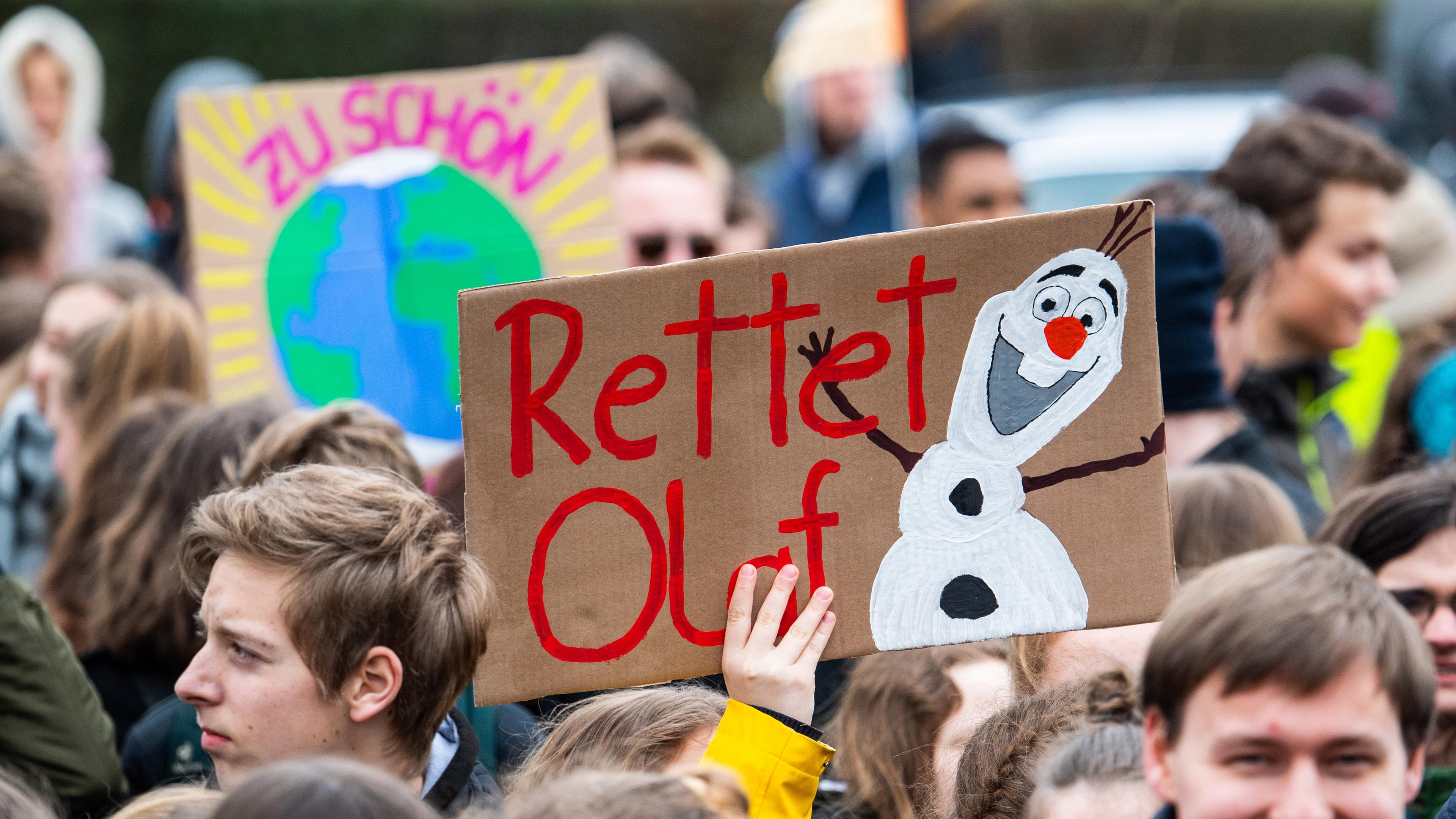 Eine Demonstrantin hält ein Schild mit der Aufschrift "Rettet Olaf", der bekannten Schneemannfigur "Olaf" aus dem Disneyfilm "Die Eiskönigin", hoch.
