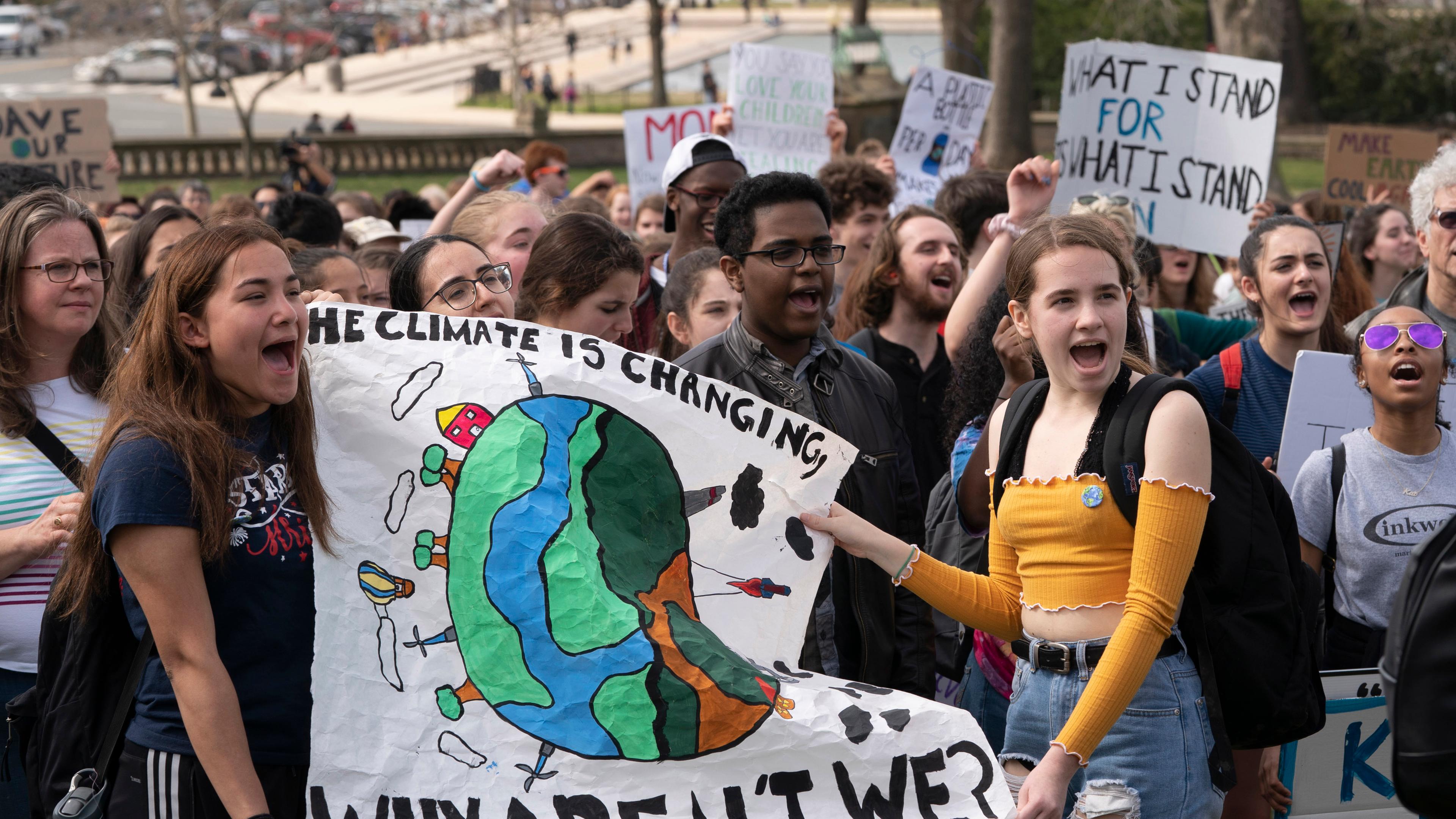 Schülerinnen halten ein Banner hoch auf dem steht: „The Climate is changing. Why aren’t we?“ (auf deutsch: Das Klima ändert sich. Warum tun wirs nicht?)