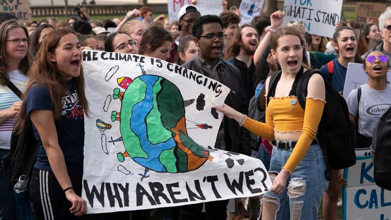 Schülerinnen halten ein Banner hoch auf dem steht: „The Climate is changing. Why aren’t we?“ (auf deutsch: Das Klima ändert sich. Warum tun wirs nicht?)