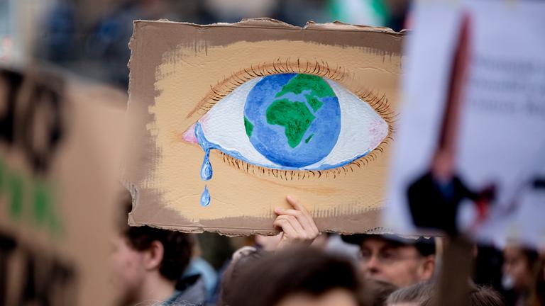 Ein weinendes Auge mit der Erde als Iris ist auf ein Plakat aufgemalt.