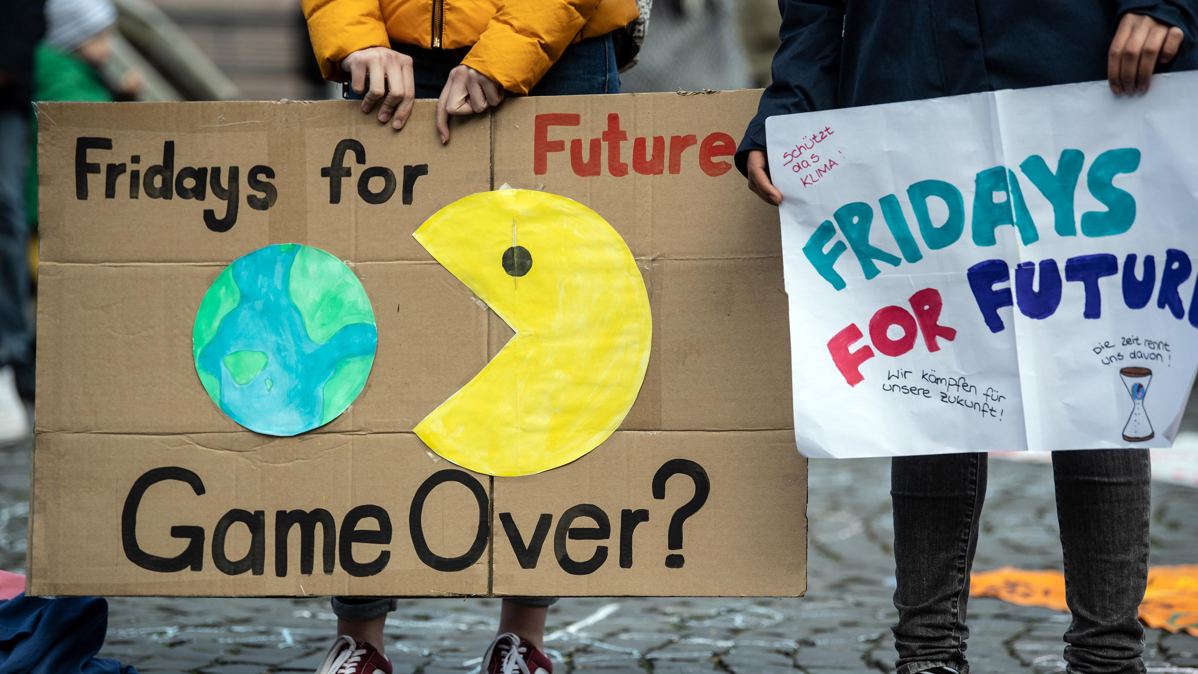 Ein Plakat auf dem die Videospielfigur "Pac-Man" nach der Erde schnappt. Darunter steht: Game Over (auf deutsch: Ist das Spiel aus?)