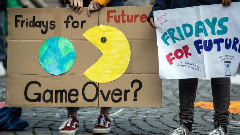 Ein Plakat auf dem die Videospielfigur "Pac-Man" nach der Erde schnappt. Darunter steht: Game Over (auf deutsch: Ist das Spiel aus?)