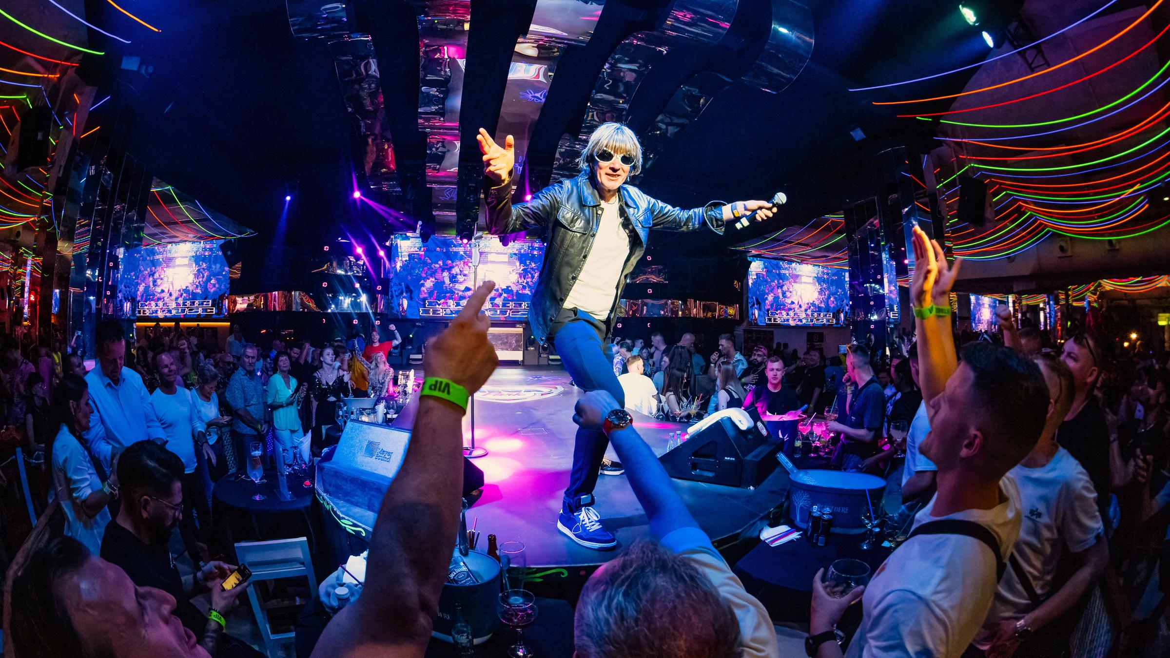 Ein Schlagersänger steht auf einer Bühne und heizt das Publikum auf Mallorca an.