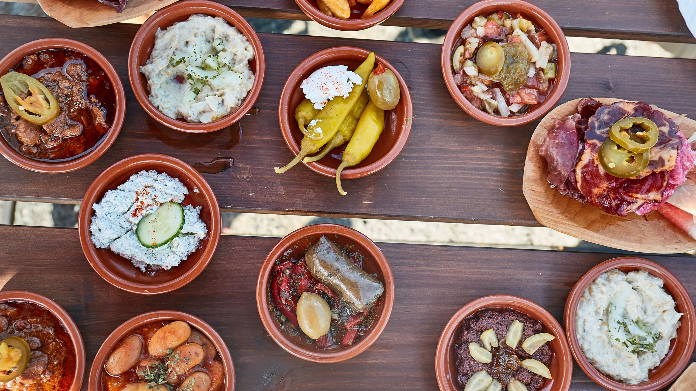 Auf einem Holztisch stehen viele kleine Schälchen mit verschiedenem Essen. Tapas sind typisch für Spanien.