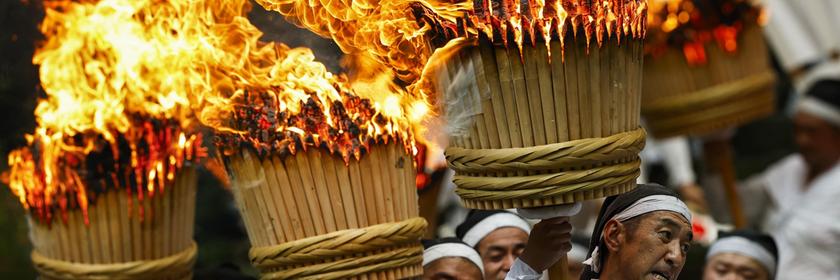 Männer in weißen Gewändern tragen riesige brennende Fackeln während eines jährlichen Feuerfestes zum Weltkulturerbe gehörenden Kumano-Nachi-Taisha-Schrein in Nachikatsuura in der Präfektur Wakayama