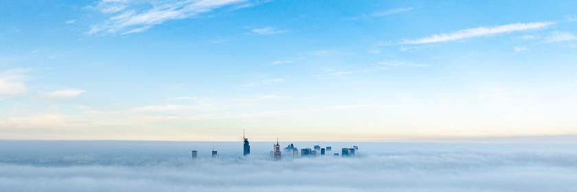 Nebel umhüllt die Skyline von Warschau, man sieht nur die Spitzen der Gebäude und darüber blauen Himmel.