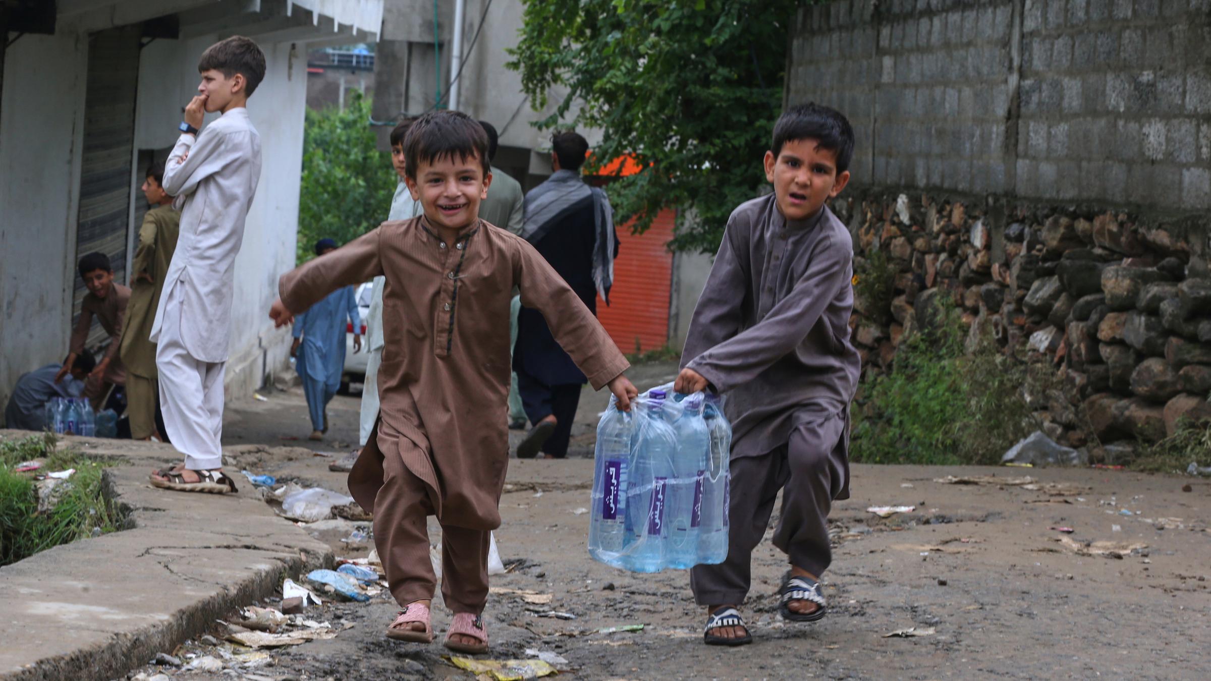 Kinder mit Wasserflaschen aus einem Hilfslager, das von Freiwilligen für die Opfer der Sturzflut am Freitag eingerichtet wurde, im Dorf Pishoreen im Bezirk Buner im Nordwesten Pakistans. 
