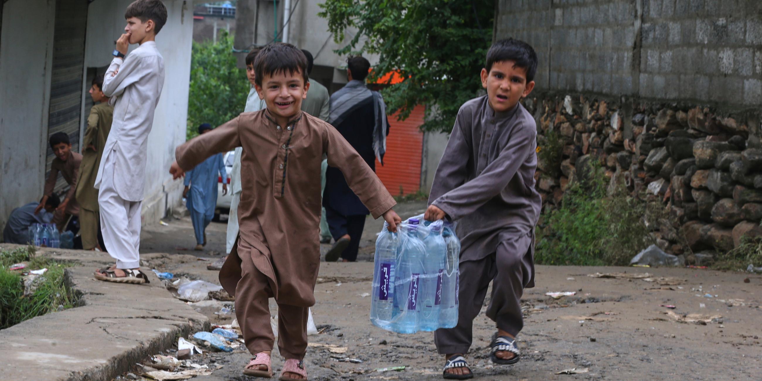 Kinder mit Wasserflaschen aus einem Hilfslager, das von Freiwilligen für die Opfer der Sturzflut am Freitag eingerichtet wurde, im Dorf Pishoreen im Bezirk Buner im Nordwesten Pakistans. 