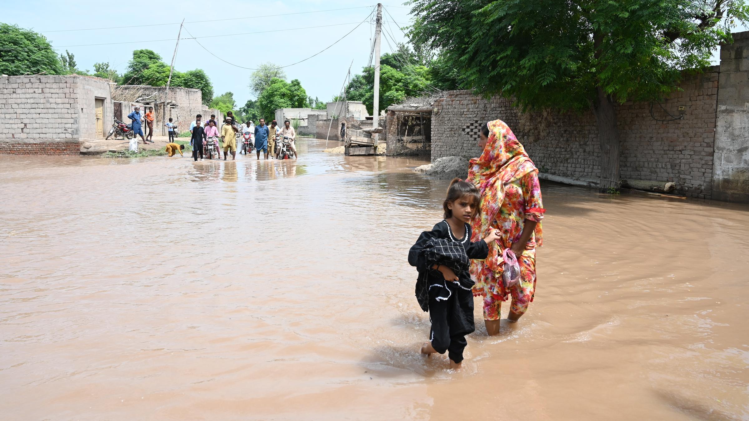 Frau mit Kind watet durch Wasser, im Hintergrund noch weitere Menschen im Wasser