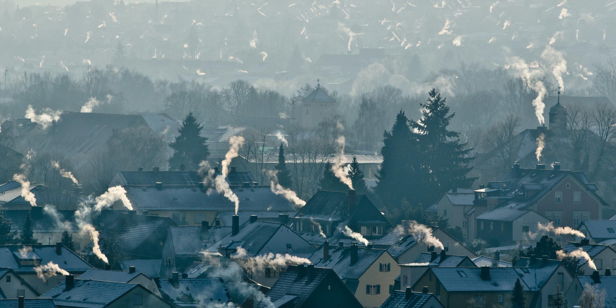 In Bayern rauchen die Schornsteine in einem Wohngebiet. Die Dächer der Häuser sind mit Schnee bedeckt.