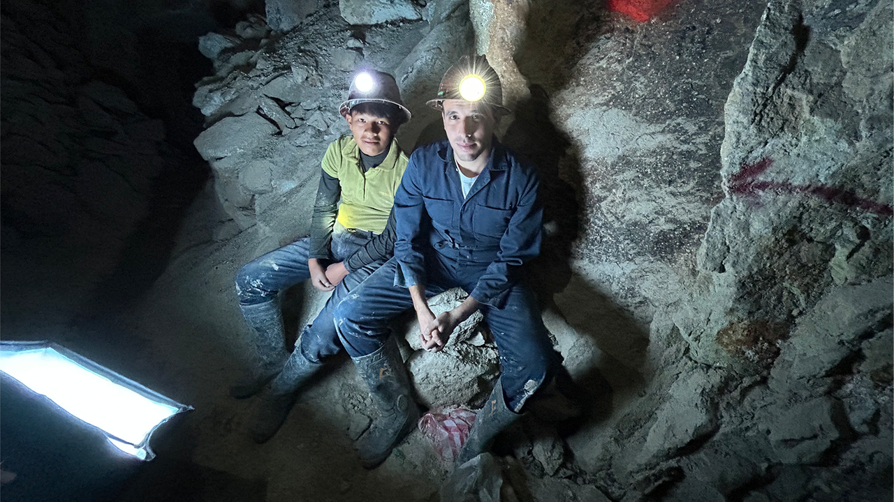 logo!-Reporter Sherif und Kind sitzen mit leuchtenden Helmlampen in Mine und schauen in die Kamera