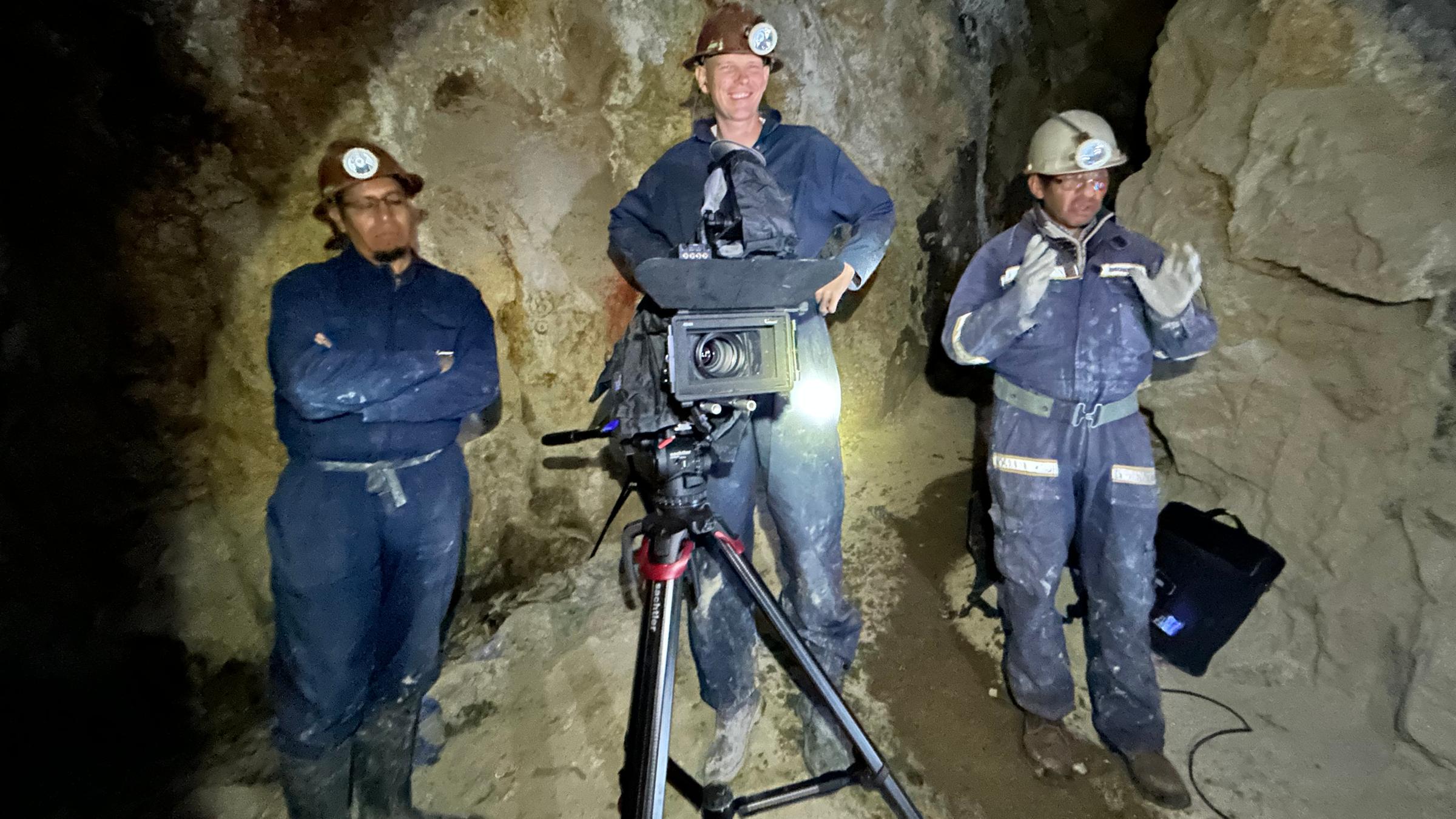 Drei Minenarbeiter stehen in Mine hinter einer Kamera