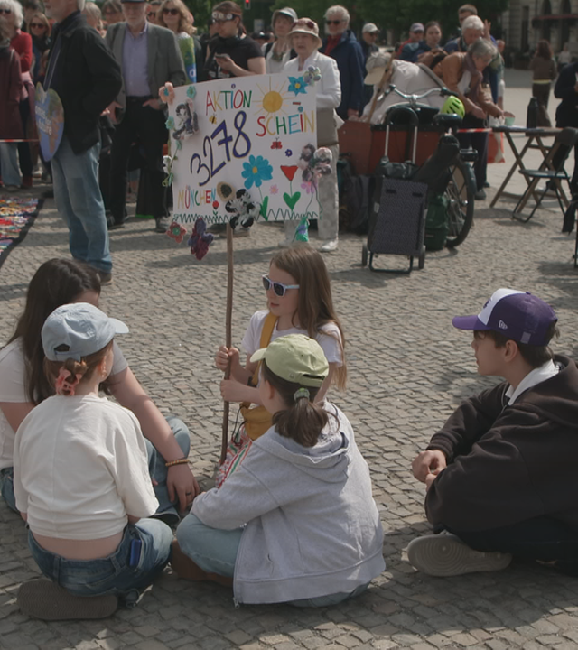 Kinder sitzen auf dem Boden; Halten Schilder; Blumen für die Umwelt