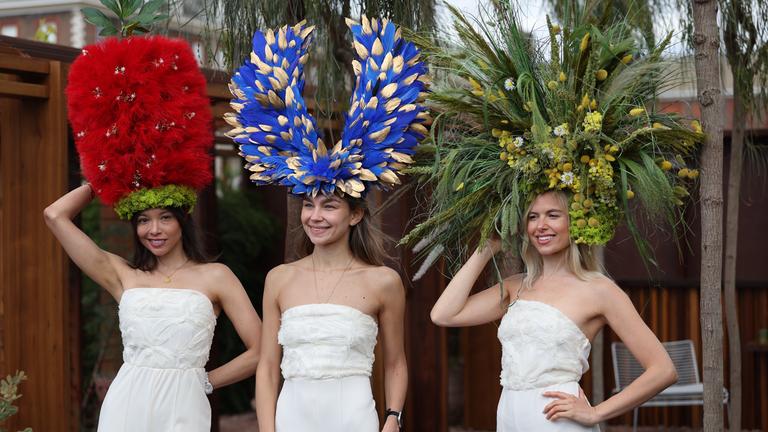Drei Models tragen riesige Hüte aus Blumen auf dem Kopf. 