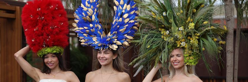 Drei Models tragen riesige Hüte aus Blumen auf dem Kopf. 