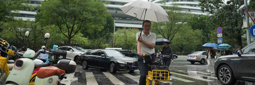 Mann hält Regenschirm in der Hand und fährt Fahrrad.