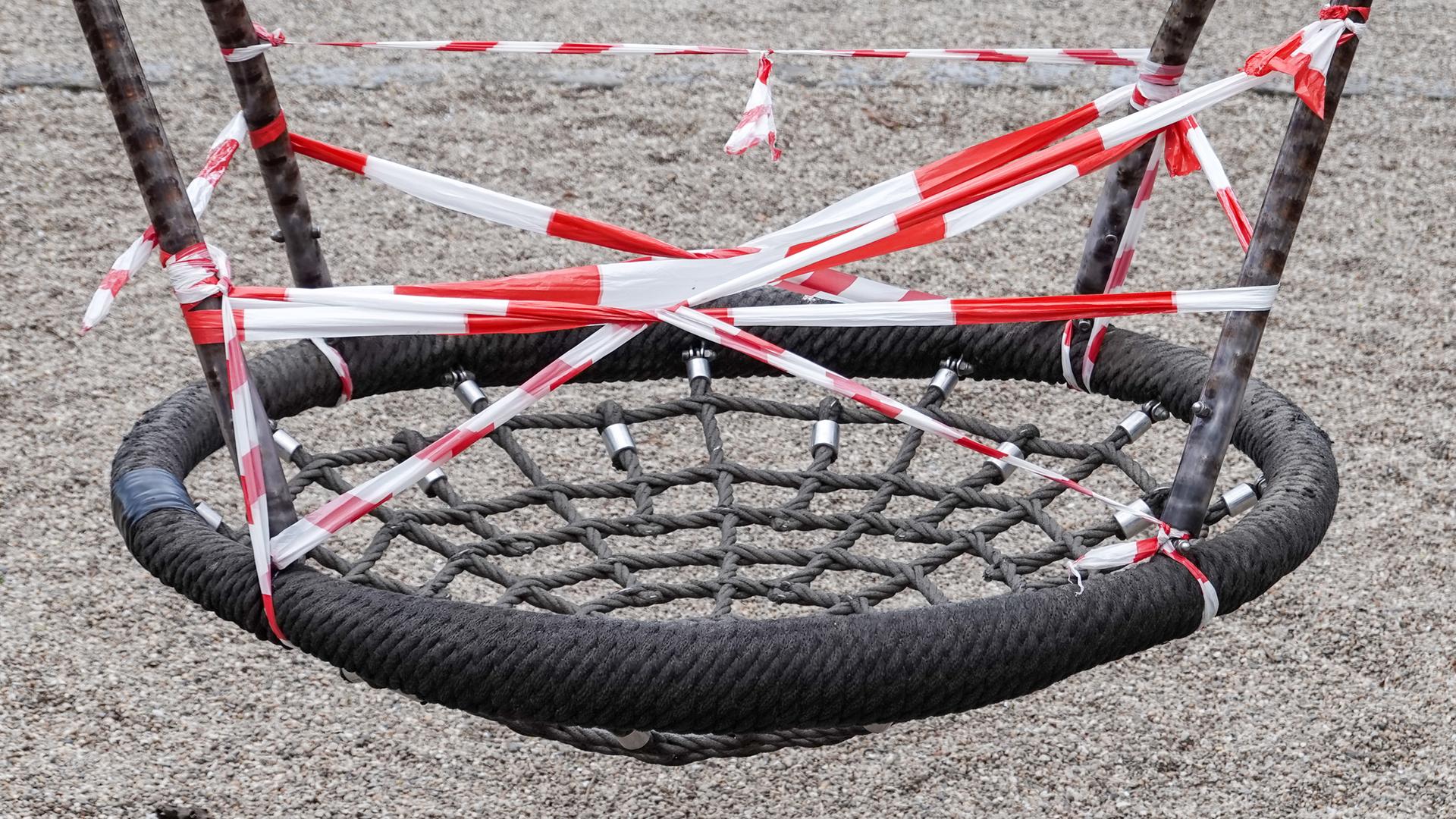 Sachsen, Leipzig: Eine Nestschaukel auf einem gesperrten Spielplatz im Leipziger Rosenthal ist mit rot-weißem Flatterband umwickelt