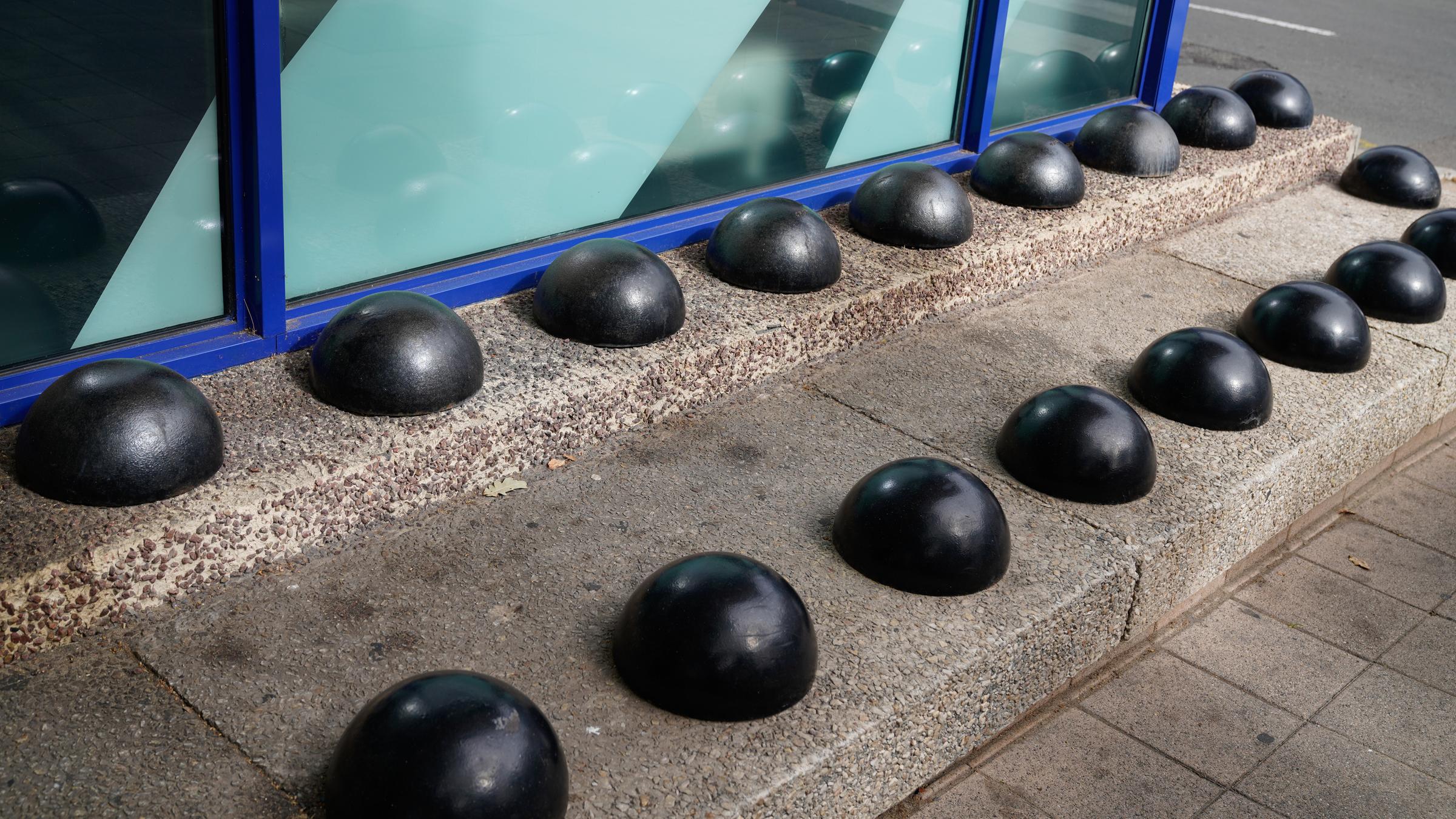 Runde schwarze Boller sind auf Stufen angebracht, sodass man sich hier nicht ausbreiten kann. 