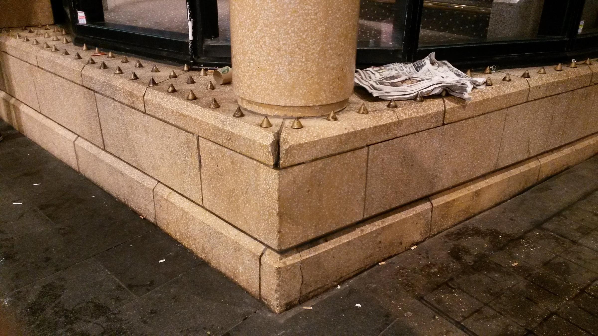 Eine Ecke von einem Gebäude in London, auf der viele kleine Metallspitzen angebracht sind. 